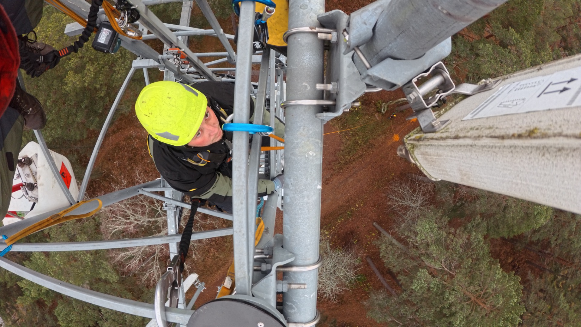 Technician in neon hard hat inspects a large metal utility structure above a grassy field.